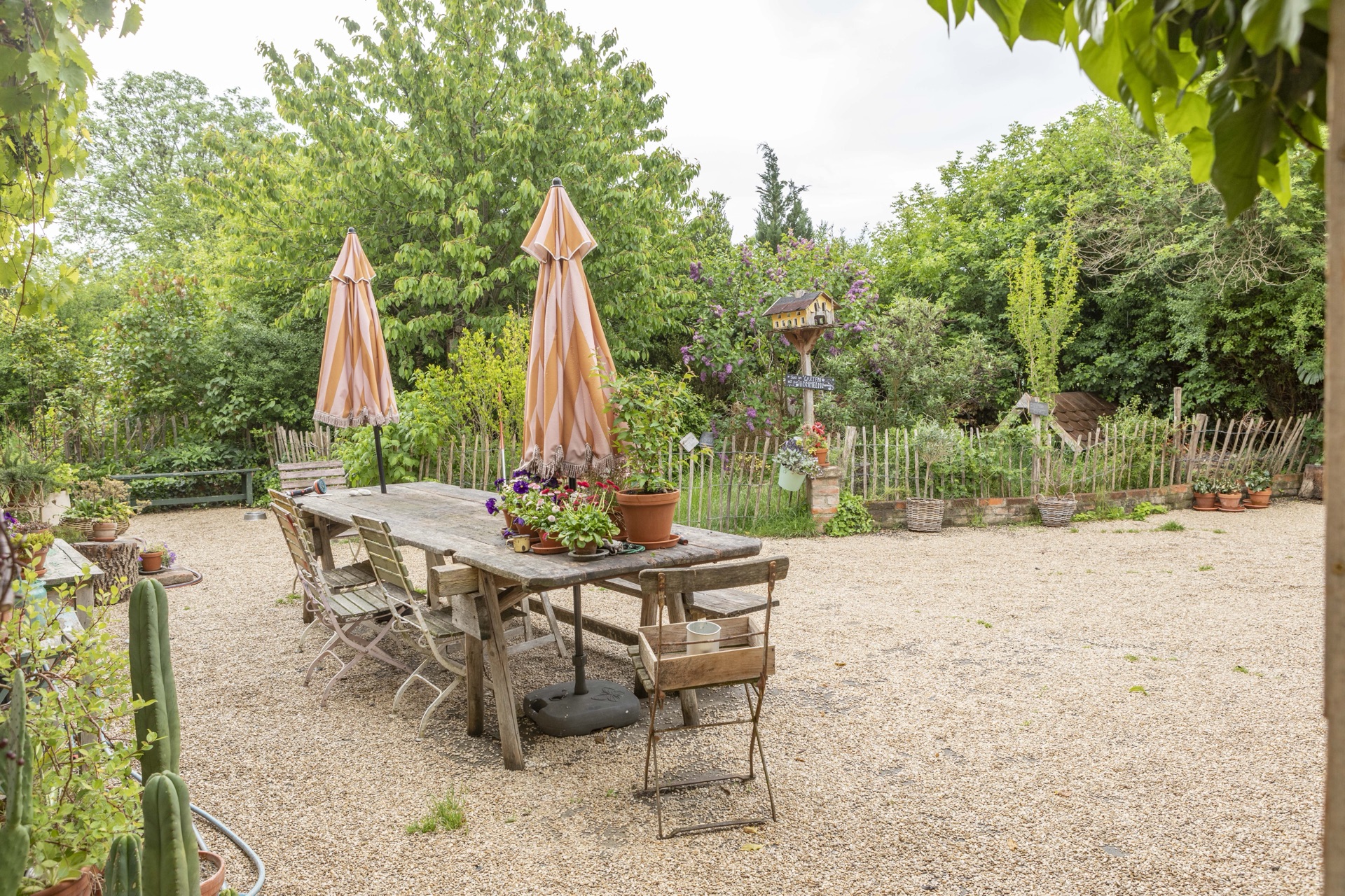 Lange Holztafel mit zusammengeklappten Sonnenschirmen und einem Vogelhaus im sommerlichen Kieshof
